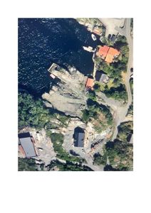 Luftfoto (satellittbilde) av et kystområde med flere bygninger, en vei og vann.