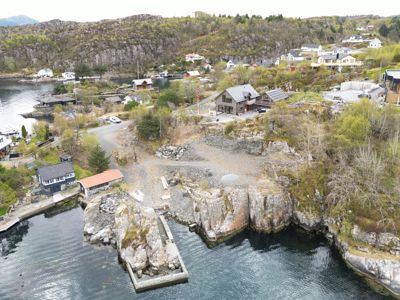 Luftfoto av et kystnær område med flere hus, en kai og omgivende natur.