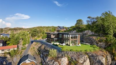 Fotografi av en moderne villa plassert på en klippete tomt med utsikt over vann og nabolag.