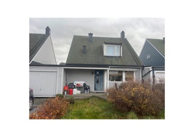 Fotografi av en eksisterende enebolig med garasje, fortau og hage.