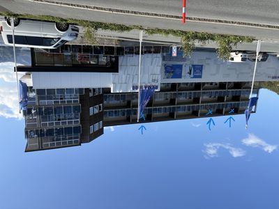 Fotografi av en eksisterende bygning (Rema 1000) med blå markeringer (pilar og kryss) som peker ut spesifikke vinduer eller balkonger.