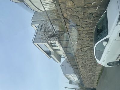 Fotografi av en moderne bygning sett fra gaten, med en steinmur og en parkert bil i forgrunnen.