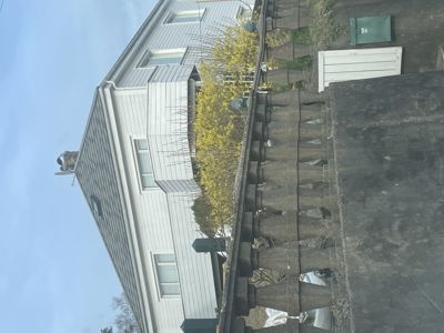 Fotografi av en eksisterende hvit husfasade sett fra siden, med en betongmur i forgrunnen.