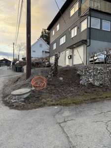 Fotografi av en eksisterende bygning sett fra siden, med tilhørende hage og vei.