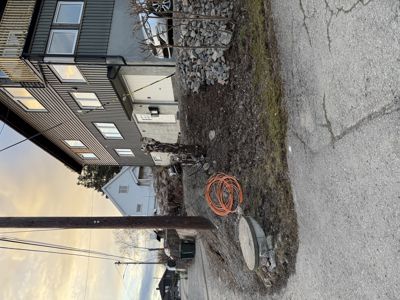 Fotografi av en eksisterende bygning (hus) sett fra siden, med synlig fasade, vinduer, en vei og omgivelser.