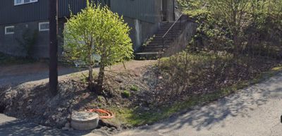 Fotografi av en bygning sett fra siden, med trapp opp til inngang, en liten trær, og en vei i forgrunnen.