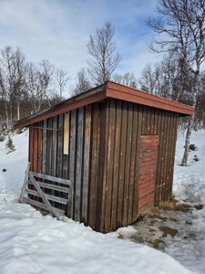 Fotografi av en liten, gammel tømmerhytte eller uthus i snø.