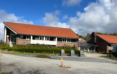 Fotografi av en eksisterende bygning med rødt tak og gjerder.