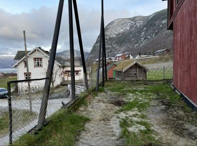 Fotografi av en bygning (eller tomte) sett fra utsiden, med nabolag og fjell i bakgrunnen.
