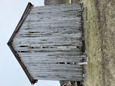 Fotografi av en gammel, utvasket trebygning (kanskje en uthus eller skur) sett fra siden.