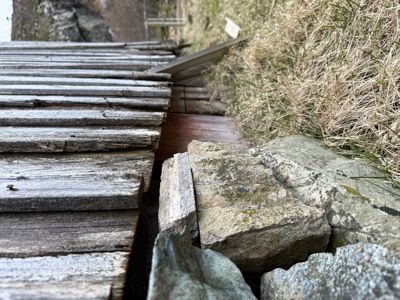 Fotografi som viser en nærbilde av en utendørs trapp eller sti laget av treplanker og steiner.