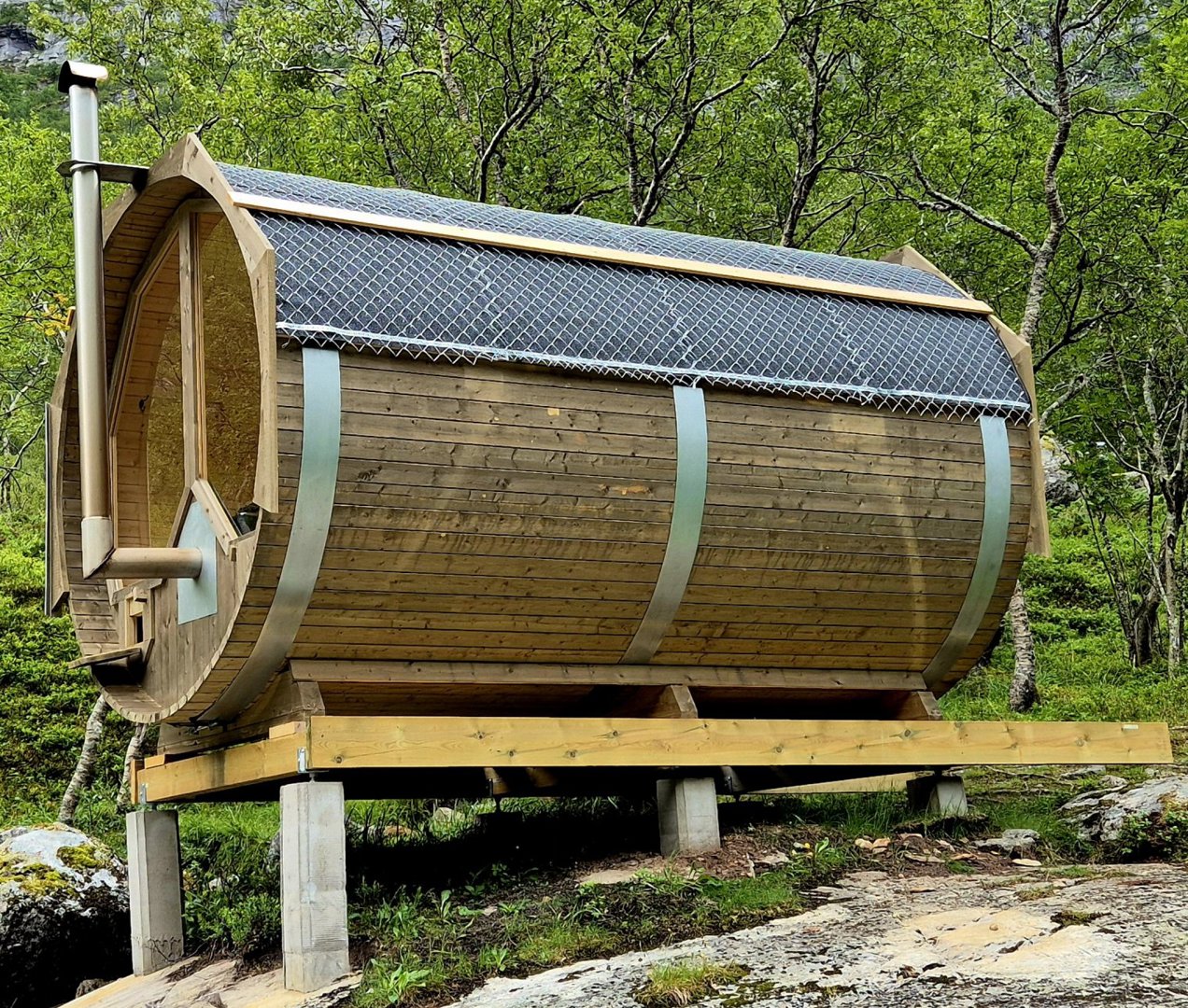 Fotografi av en ferdigbygd, sylindrisk trehytte (trollhytte) med solpaneler på taket, stående på betongfundament i et skogsmiljø.