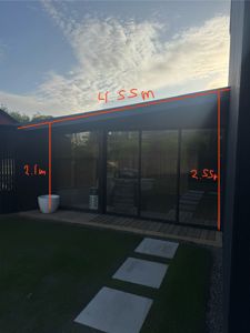 Fotografi av en moderne utvendig fasade med glassdører og en terrasse, med håndtegnede mål på 4,55 m, 2,1 m og 2,55 m.