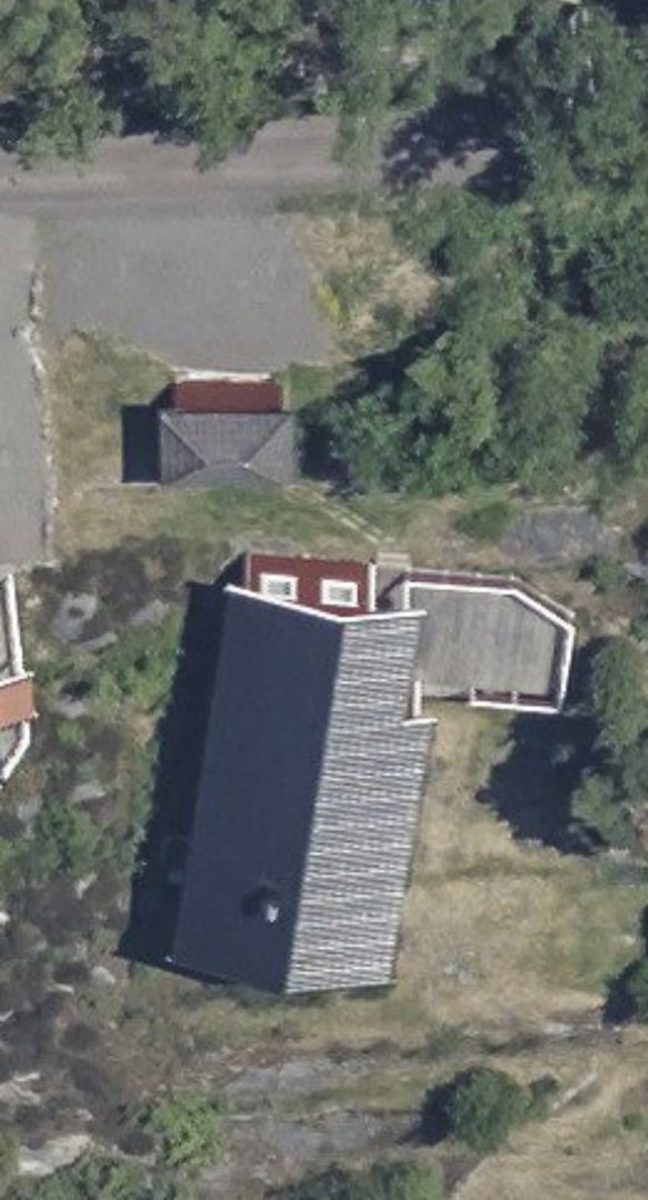 Luftfoto av en tomt med en hovedbygning, en mindre uthusbygning, en bilplass og omgivende natur.