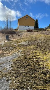 Fotografi av en gul bygning (borettslag eller privat hus) sett fra et lavt nivå oppover mot bakken.
