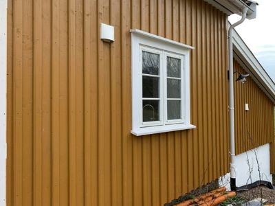 Fotografi av en fasade på en bygning med gule paneler, et hvitt vindu, en nedløpsrør og en utendørs lysarmatur.