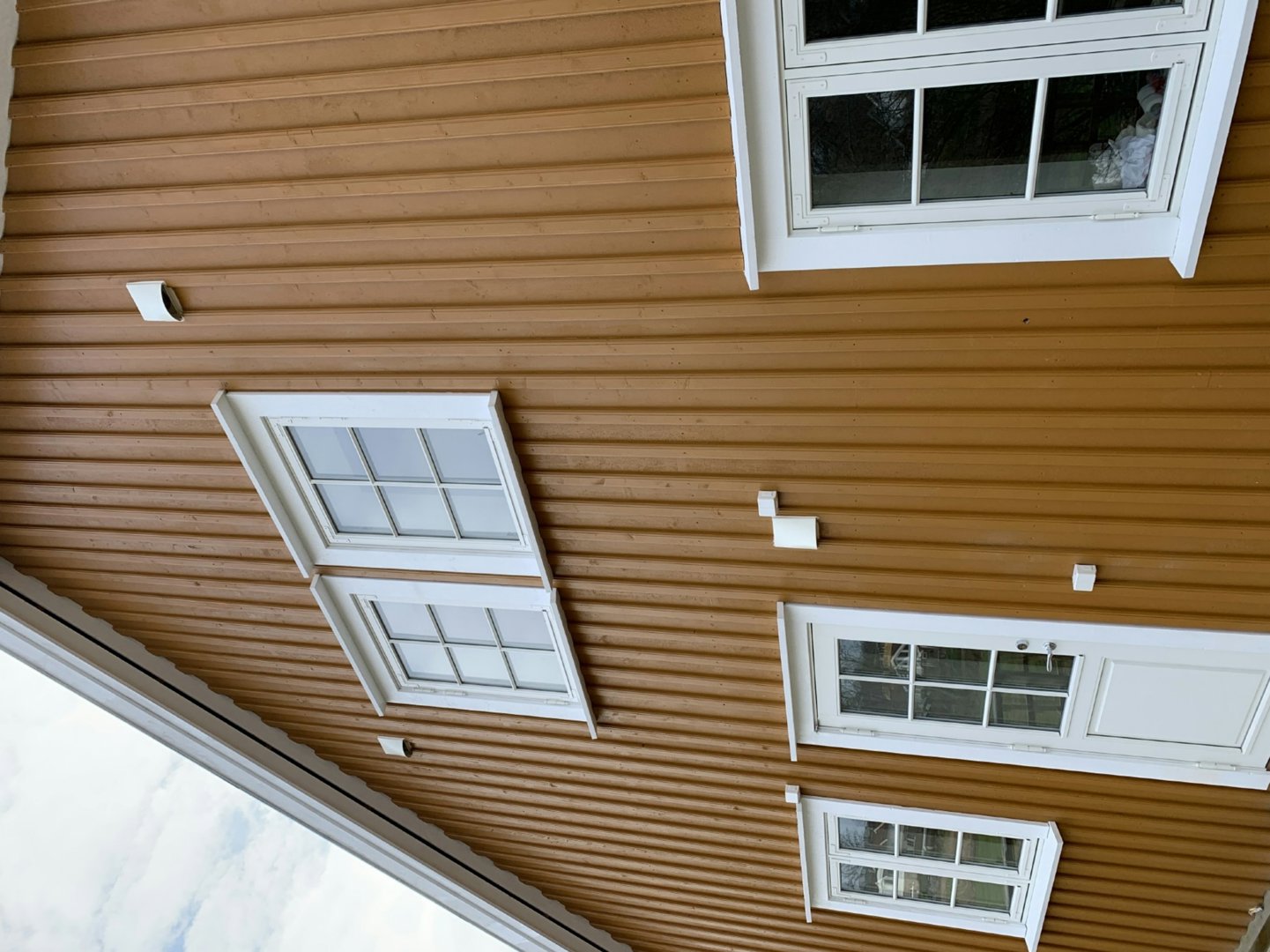 Fotografi av fasaden på en bygning med brun panelvegg, hvite vinduer og lysarmaturer.