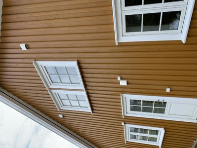 Fotografi av fasaden på en bygning med brun panelvegg, hvite vinduer og lysarmaturer.