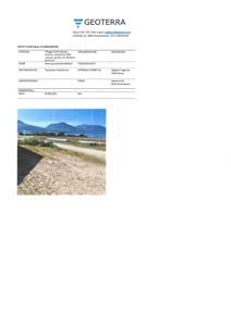 Fotografi av et terreng med en sti, vegetasjon og fjell i bakgrunnen, inkludert en del av en bygning eller struktur til høyre.