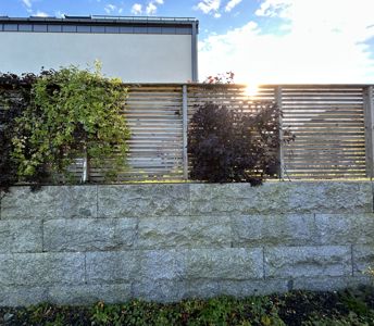 Fotografi av en fasade med en steinmur, en trepanelgjerde og en bygning i bakgrunnen.