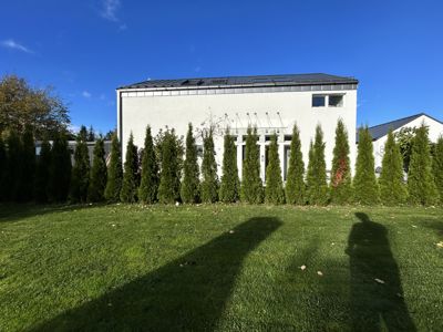 Fotografi av en hvit bygning sett fra bakgård eller hage, med en rekke tuer foran.