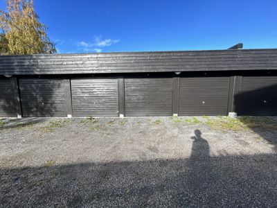 Fotografi av en rekke med garasjer med mørke dører og en grusplass foran.