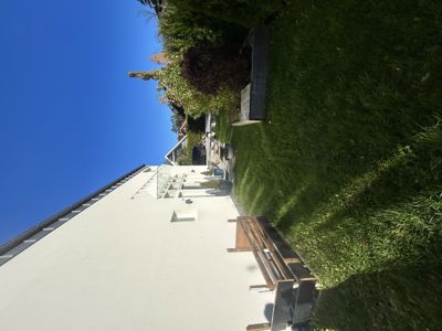 Fotografi av en hvit bygning sett fra siden, med en benk og gressområde i forgrunnen.