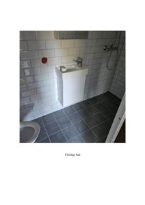 Fotografi av et fliselagt bad med hvite fliser, en vask og dusj.