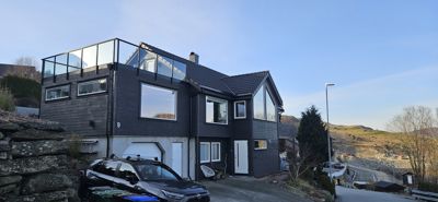 Fotografi av en moderne, mørk fasade med store vinduer og et glassdekket takterrasse.