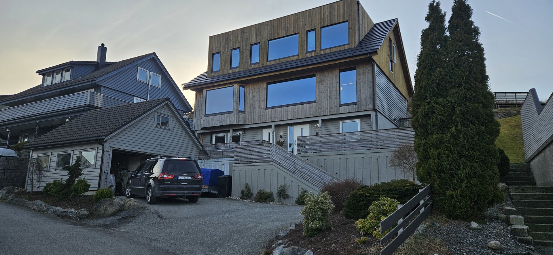 Fotografi av en moderne villa med trepanel og store vinduer, sett fra gaten.