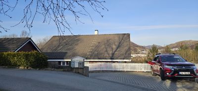 Fotografi av en bolig med tak, hekk og bil foran.