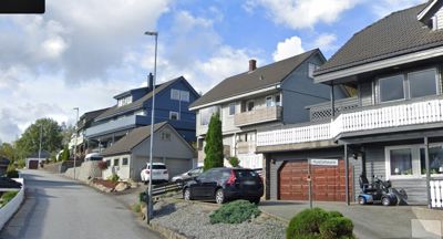 Fotografi av en gate med flere bolighus, parkerte biler og billett.