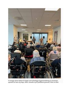 Fotografi av en innendørs konsert eller arrangement i et rom med publikum i rullestol.