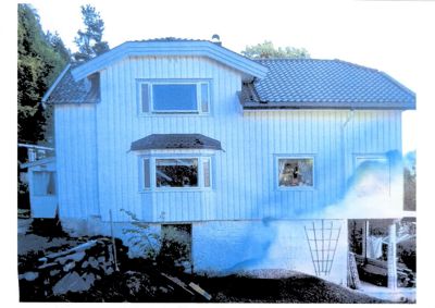 Fotografi av en eksisterende, hvitmalt trehus med tak og vinduer.