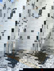 Fotografi av en hvit, panelt fasade på en bygning med vinduer og en åpen inngangsdør. Bildet viser også en delvis nedmontert eller midlertidig planket terrasse med snø på bakken.