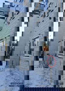 Fotografi av fasaden på en bygning sett fra bakken, med snø på bakken og et rødt sirkelmerke som peker på en detalj ved vinduet.