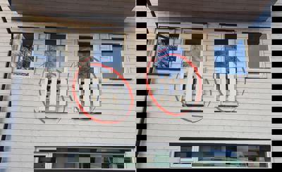 Fotografi av fasaden på en bygning med hvite lister og vinduer, der to vinduer er markert med røde sirkler.