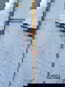 Fotografi av en fasade med snø, der en målebånd og en rød sirkel markerer et spesifikt punkt på veggen.