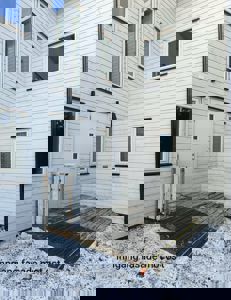 Fotografi av en bygning med hvit panelvegg, vinduer og en inngangsdør mot øst.