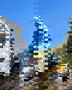 Fotografi av en byggeplass med en hvit villa, en gullgraver (Komatsu) og en lastebil i bakgrunnen.