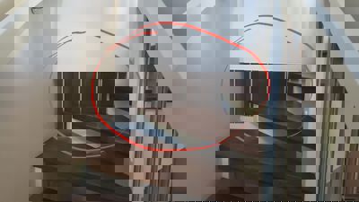 Fotografi av en trapp med mørke tretrinn og metallstolper, der et rødt sirkel er tegnet rundt en del av veggen under trappen.