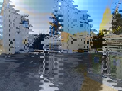 Fotografi av en nybygd hvit villa sett fra siden, med en oppkjørsel og en søppelstasjon i forgrunnen.