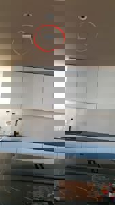 Fotografi av en moderne kjøkkeninnredning med hvite skap, mørk benkeplate og innbygget komfyr. Bildet viser også en del av taket med en lysarmatur.