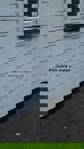 Fotografi av en hvit, panelt fasade med et vindue og en svart sokkel. Bildet har teksten 'Fasade mot vest' på seg.