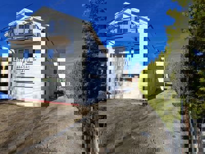 Fotografi av en hvit villa med balkong og garasje, sett fra siden under blå himmel.