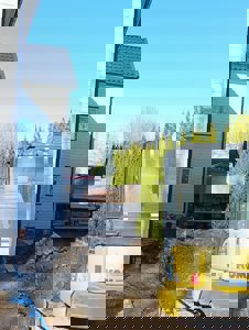 Fotografi av en byggeplass med en grå husvegg til venstre, en lastebil i bakgrunnen og en gullig gummigraver (KOM) i forgrunnen.