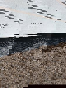 Fotografi av bygningens nederste del mot vest, som viser hvite fasadeskiver, en svart fuktbarriere med knopper, og jord i forgrunnen.