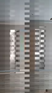 Fotografi av et tomt rom med lyse gulv og vegger, med utsikt gjennom en døråpning til en gang og et vindu.