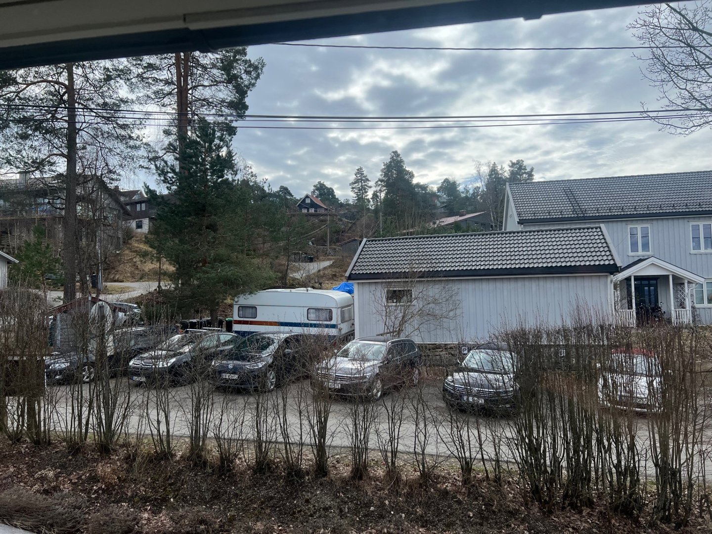 Fotografi av en boligbebyggelse med parkeringsplass, bilvogner og omgivende natur.