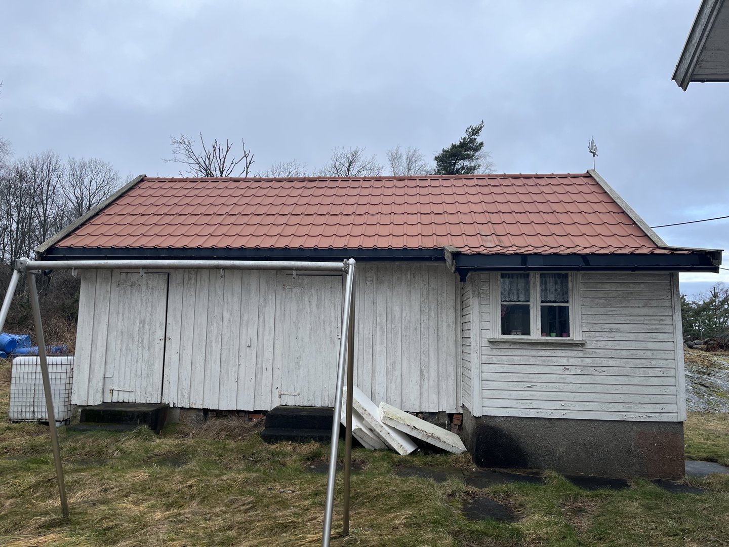 Fotografi av en liten, hvit malte hytte med rødt tak sett fra siden.